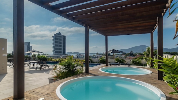 Un espace piscine sur le toit, comprenant deux bains à remous, des pergolas en bois et une vue sur le paysage urbain et les montagnes.