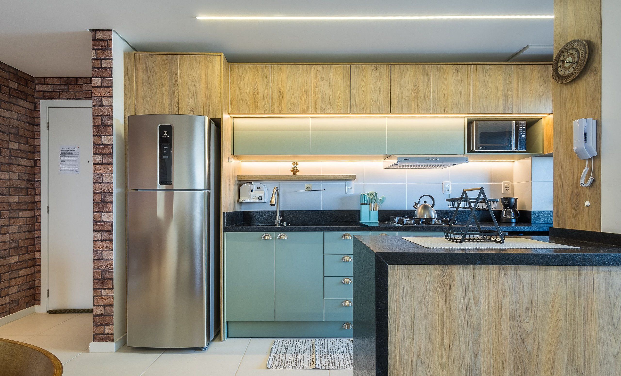 A modern kitchen with a stainless steel refrigerator, wooden cabinets, a microwave, and a coffee machine.
