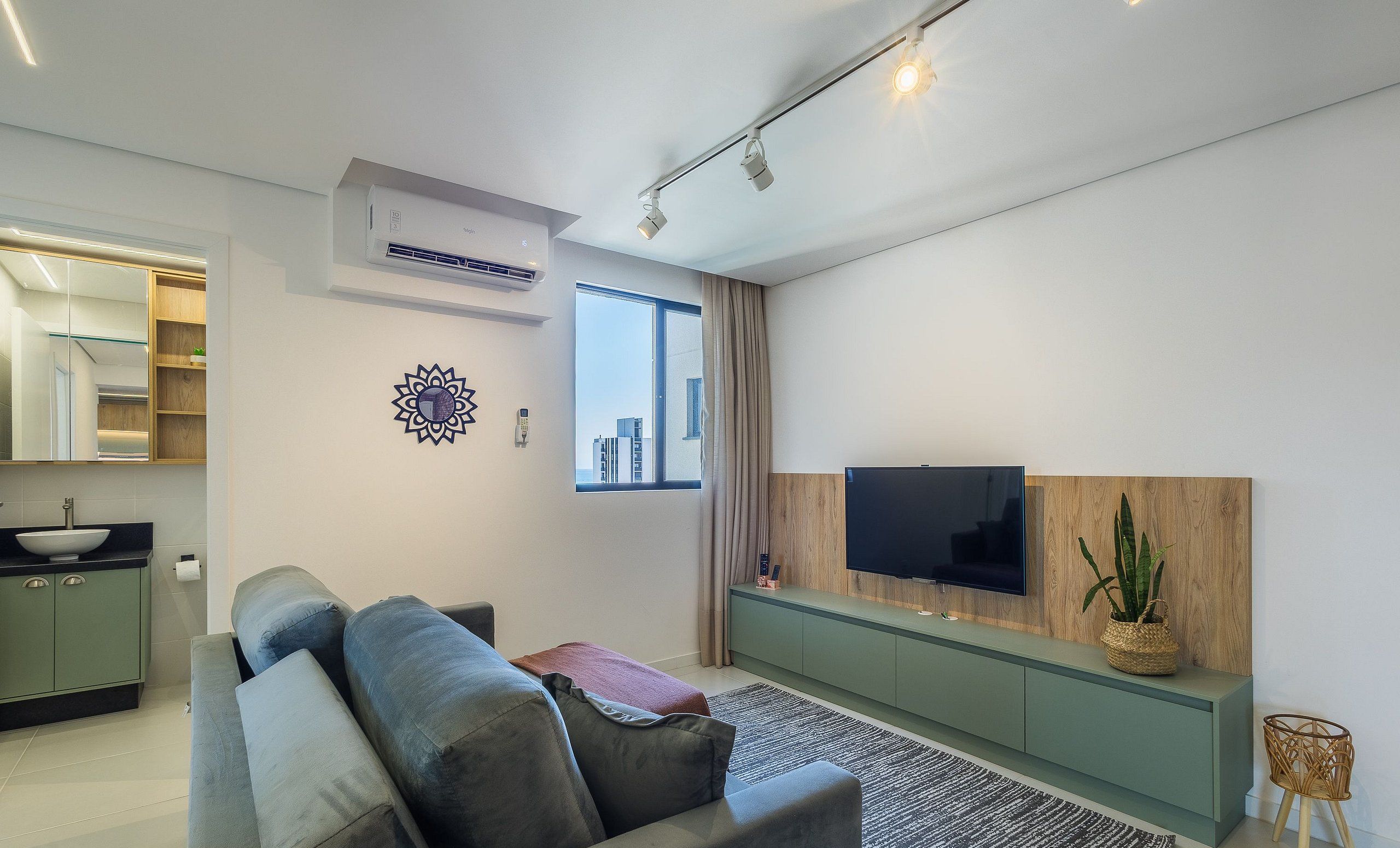Een moderne woonkamer met een bank, televisie, airconditioning en uitzicht op de stad.