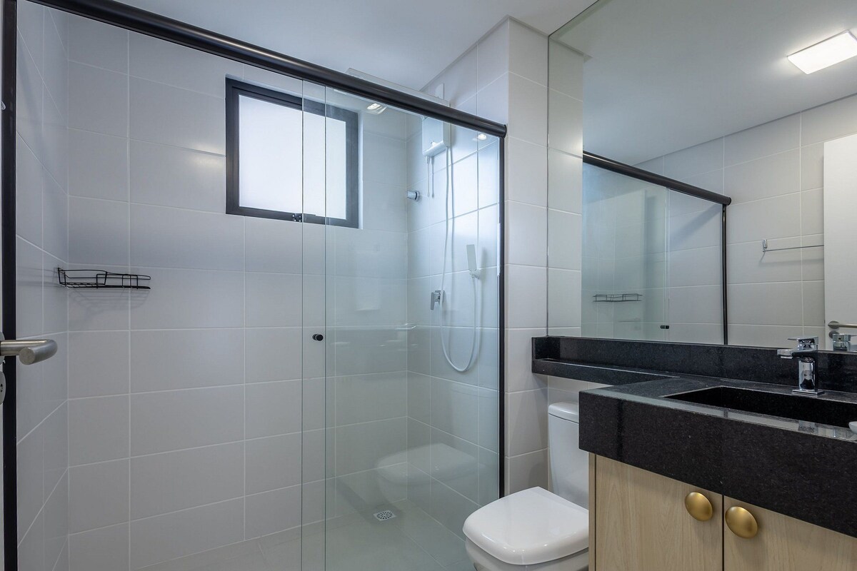 Une salle de bain moderne avec une douche à l’italienne en verre, des toilettes, un lavabo doté d’un plan de travail noir et un miroir.
