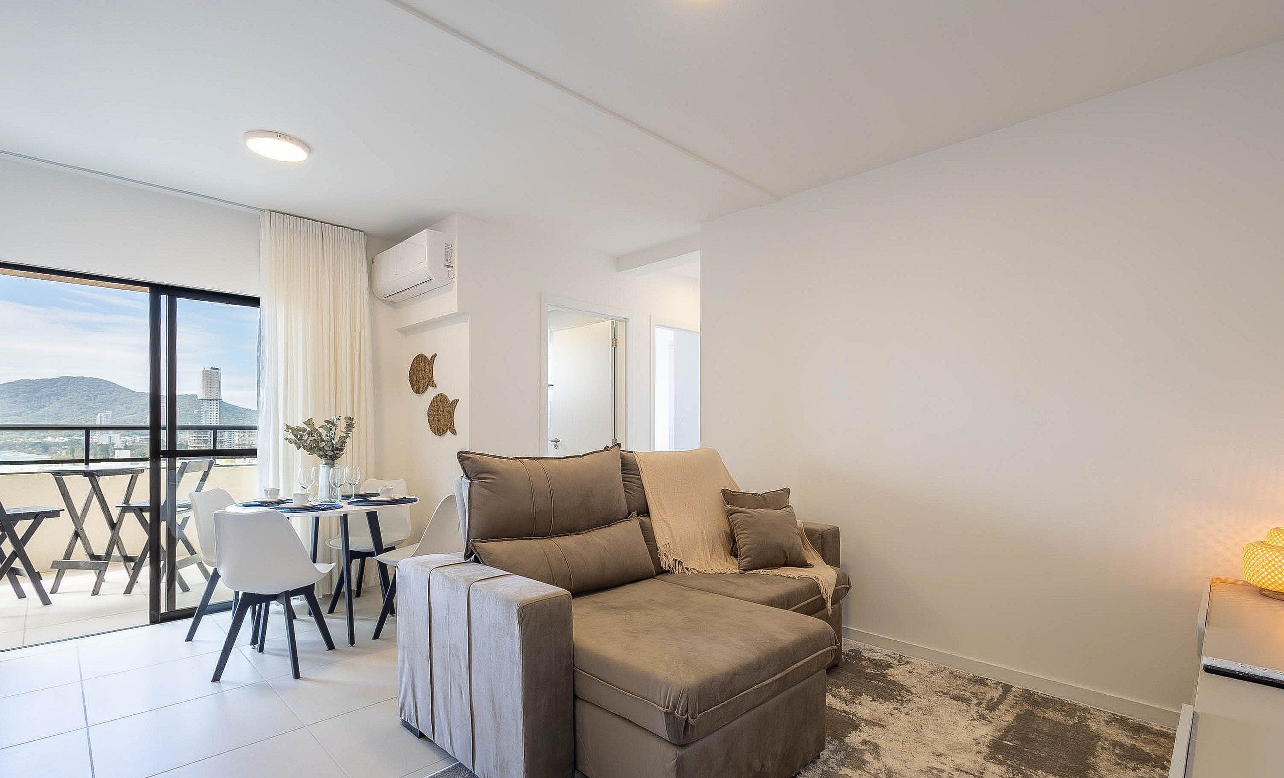 Sala de estar moderna com sofá, mesa de jantar com cadeiras e uma grande janela com vista para a cidade.