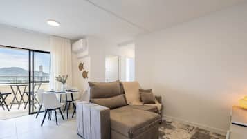 A modern living room with a sofa, a dining table with chairs, and a large window offering a city view.