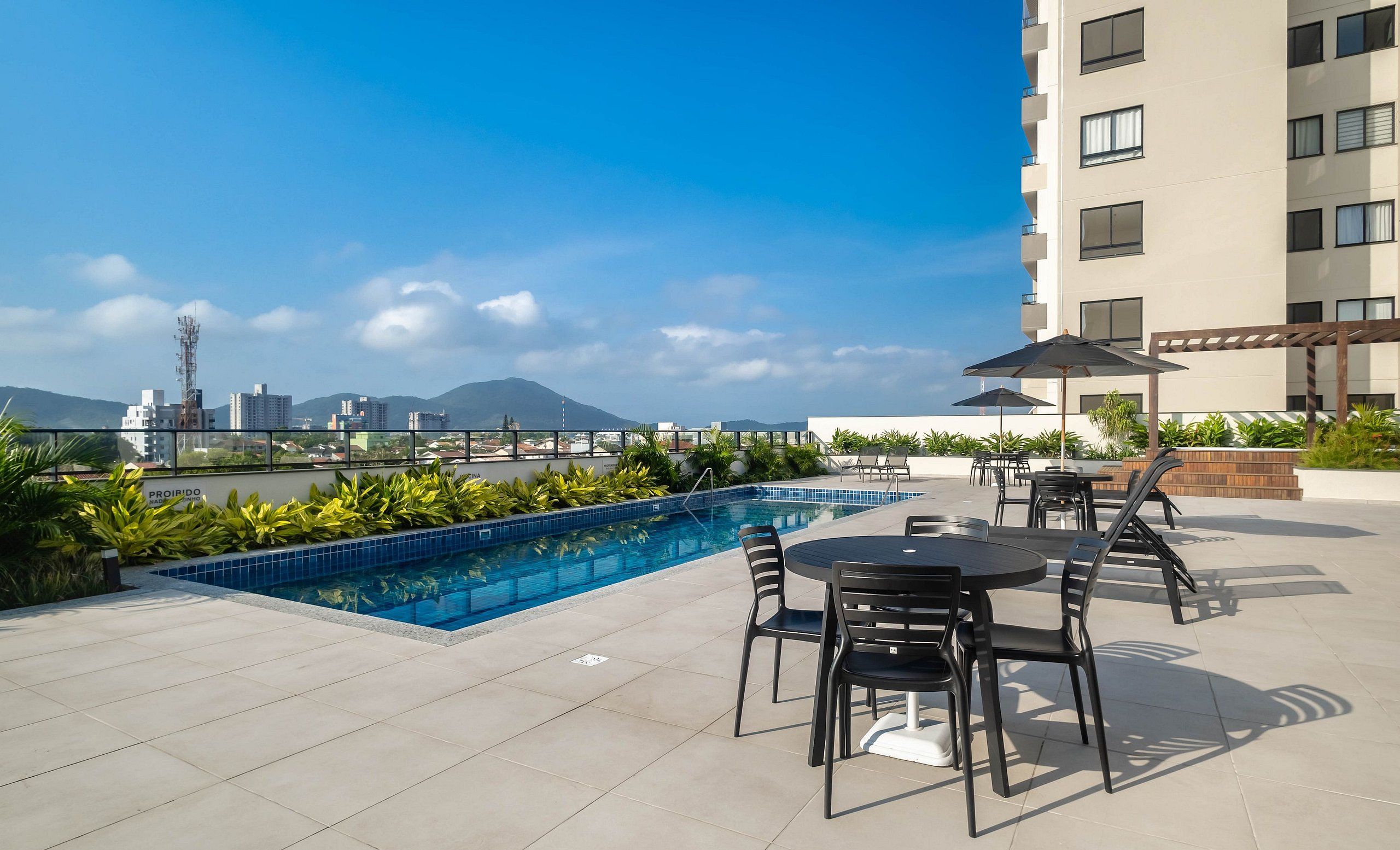 A rooftop pool with a cityscape view, outdoor seating, and a modern building in the background.