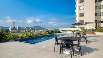 A rooftop pool with a cityscape view, outdoor seating, and a modern building in the background.