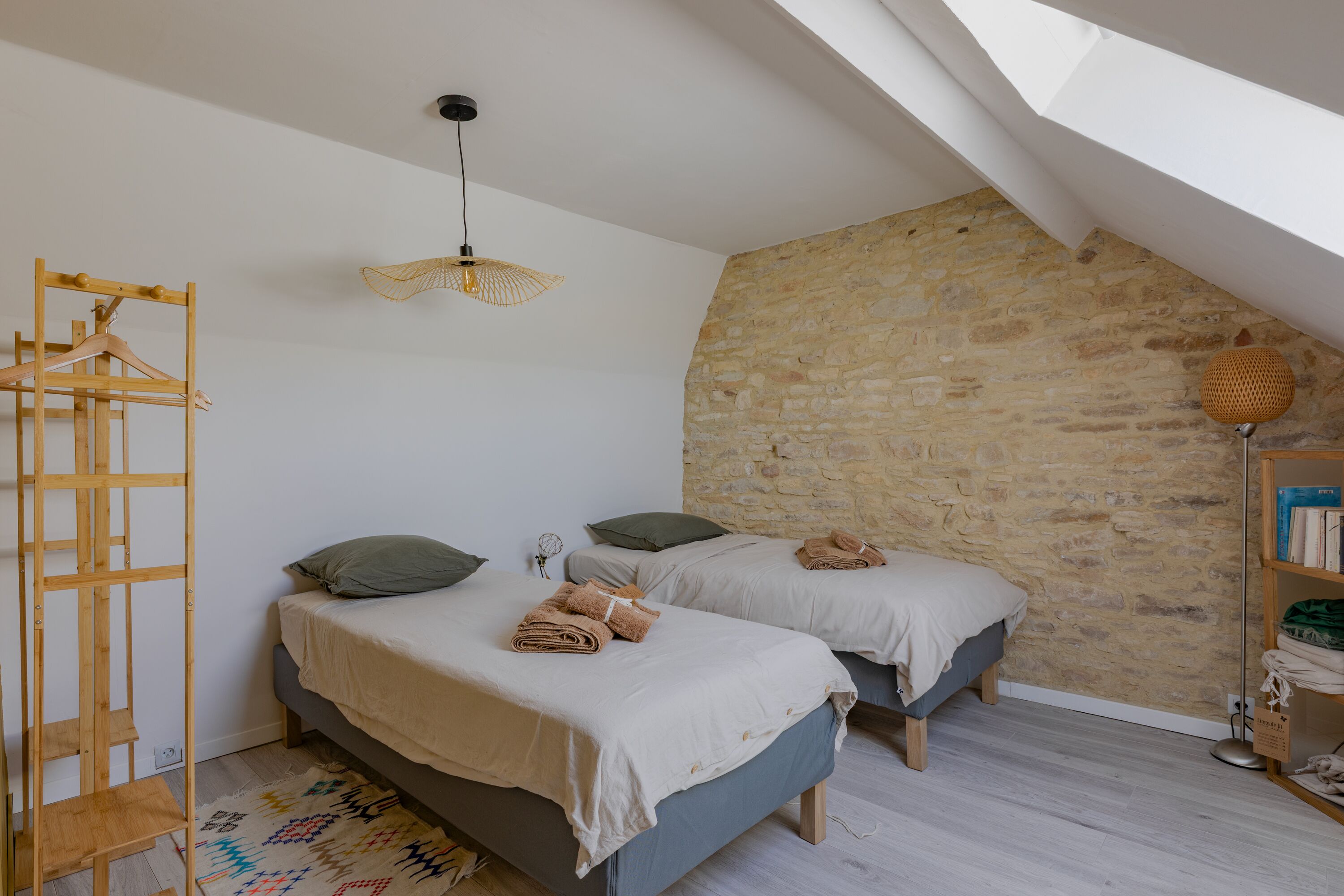 A bedroom with two beds, a wooden ladder, a stone wall, and a hanging light fixture.
