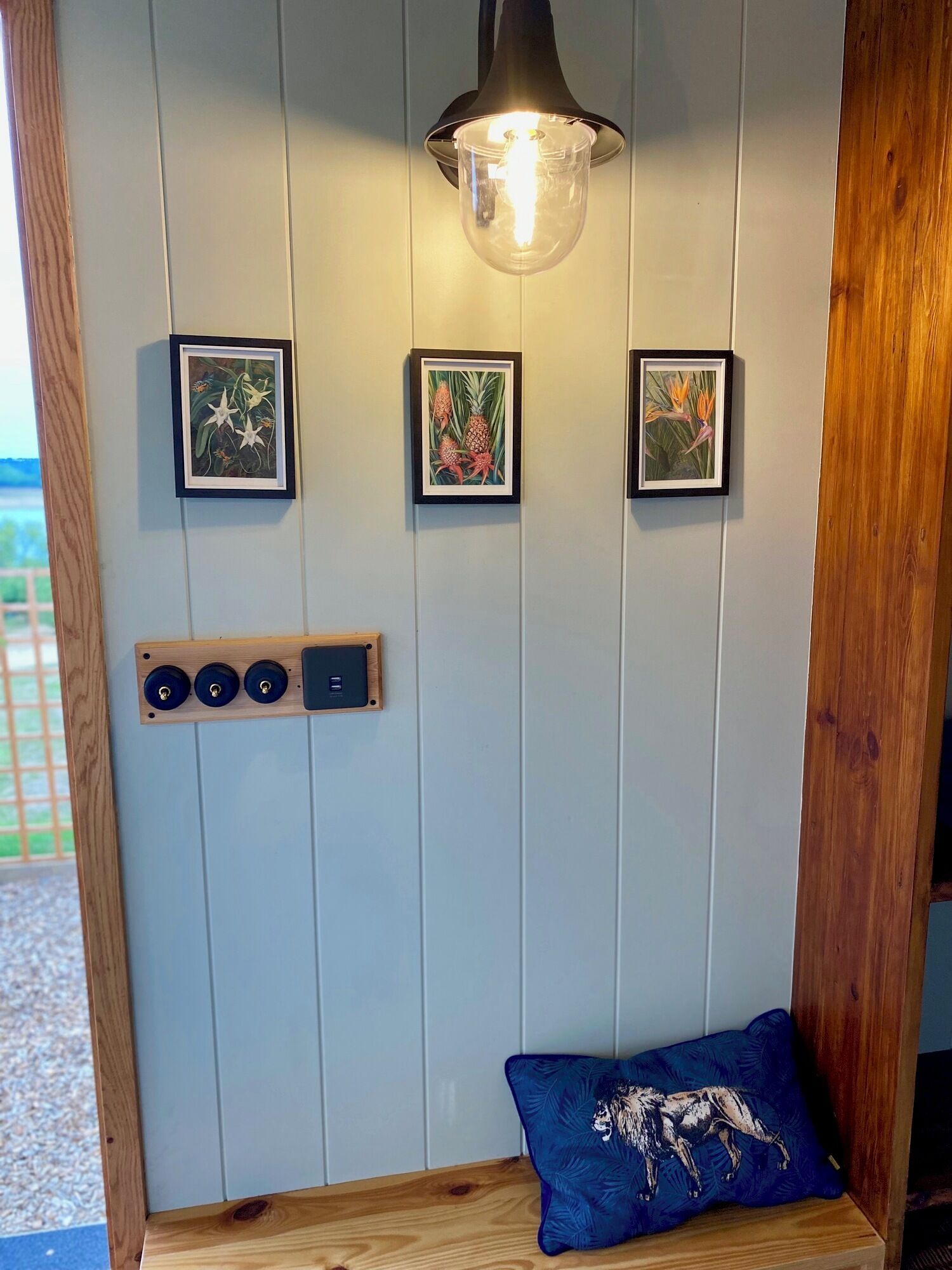 A room with a wooden bench, a wall-mounted light fixture, and three framed botanical prints.
