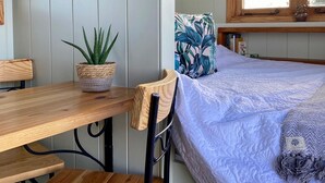 Een gezellige kamer met een houten tafel en stoelen, een bed met een decoratief beddegoed, een potplant en een raam met gordijnen.