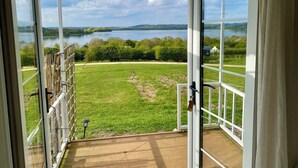 A view from a covered deck with glass doors, overlooking a grassy area and a lake.