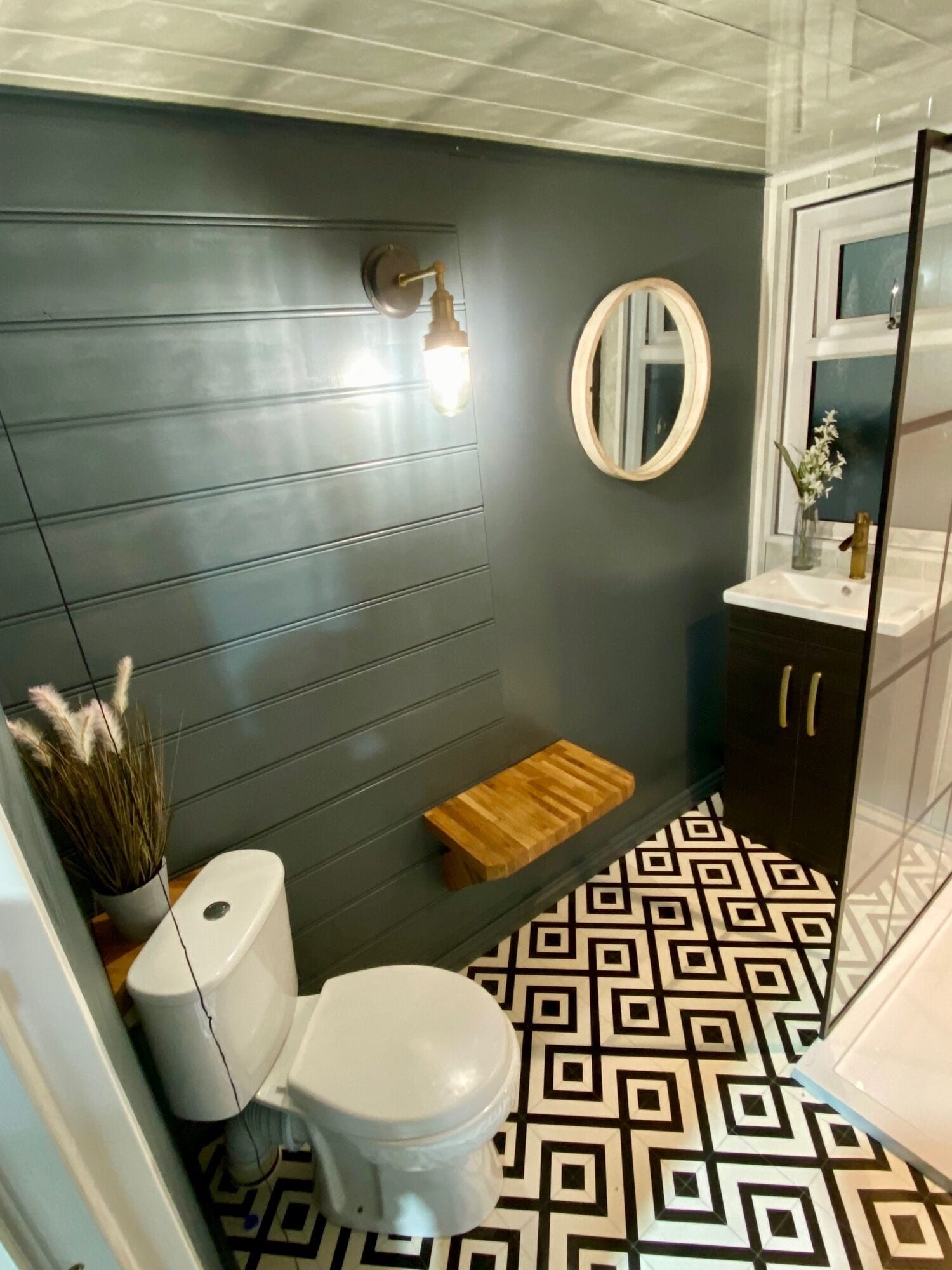 Een badkamer met een modern design, met een grijze wand, een wit toilet, een houten plank, een spiegel en een vloer met een patroon.