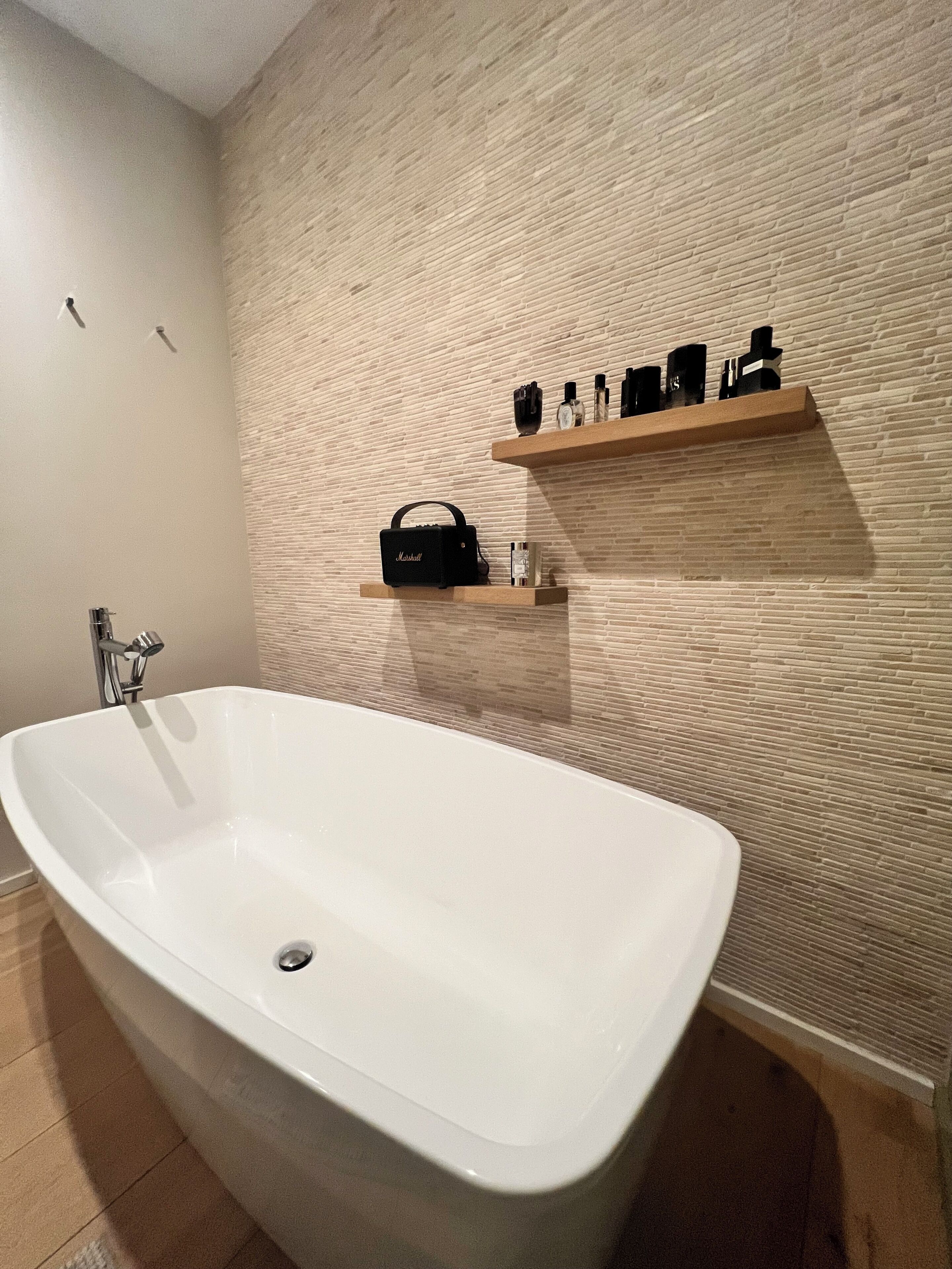 A bathroom with a freestanding bathtub, a wooden shelf with toiletries, and a textured wall.