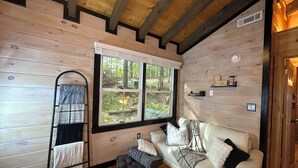 A cozy cabin interior with a wooden floor, a sofa with cushions, a window with blinds, and a towel rack.