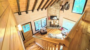 A wooden cabin interior with a stone fireplace, a mounted moose head, and a large window.