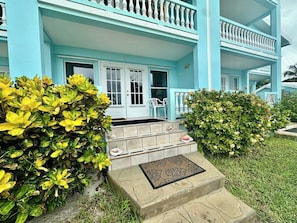 A two-story building with a light blue exterior, a front porch with a white railing, and a set of stone steps leading to the entrance.