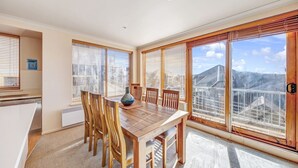 A dining area with a wooden table and chairs, large windows with blinds, and a view of a mountain. - Schnapps 3 - Mt Hotham (Hotham Heights)