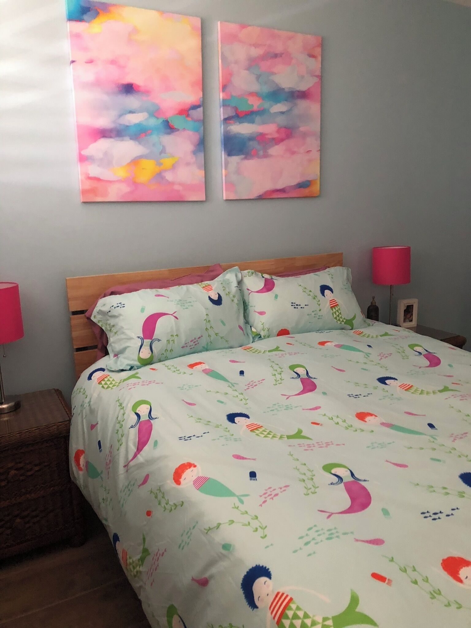 A bedroom with a bed, two bedside lamps, and abstract wall art.