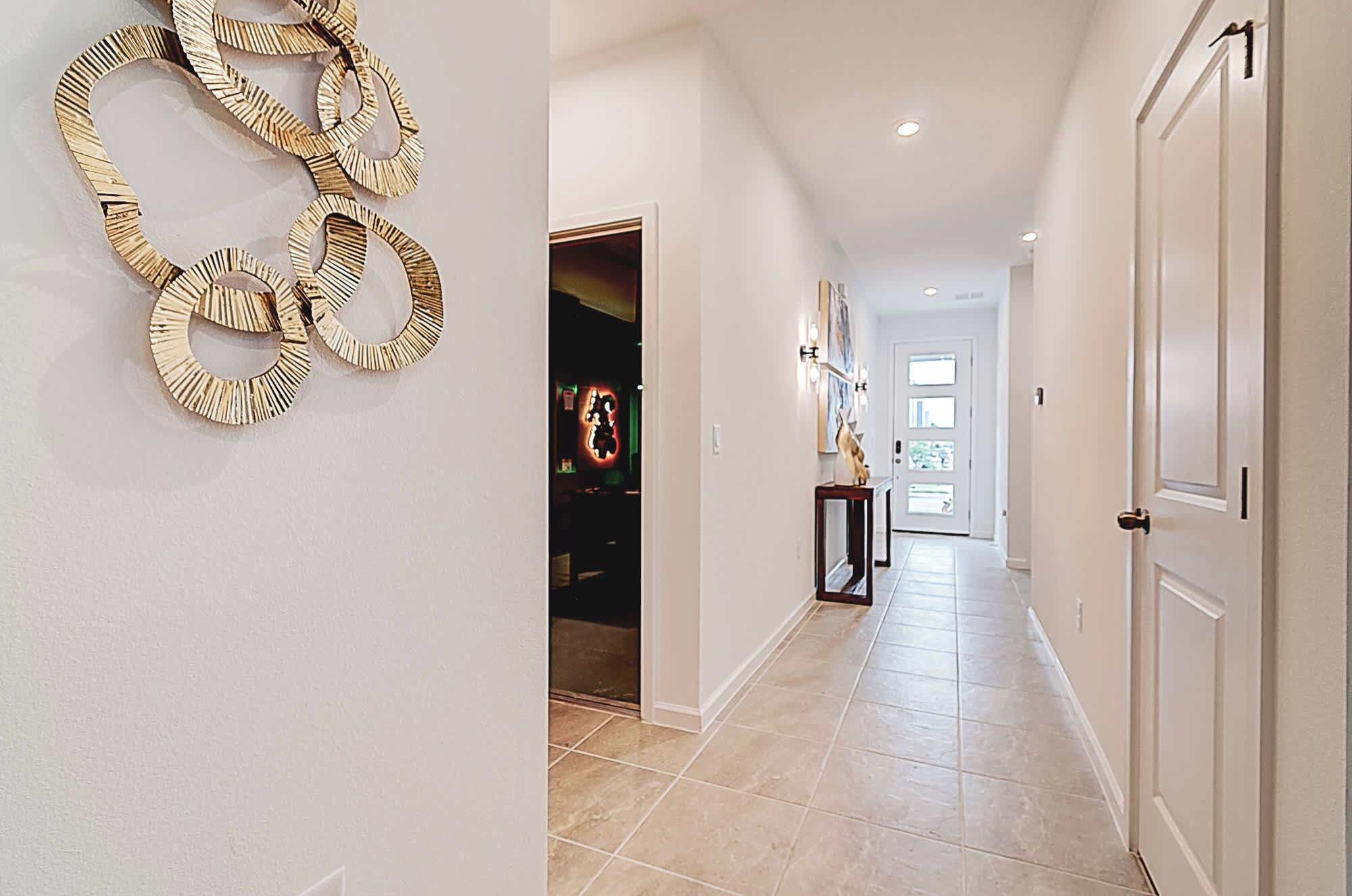 A hallway with a tiled floor, a door on the right, and a wall with a circular decorative piece.
