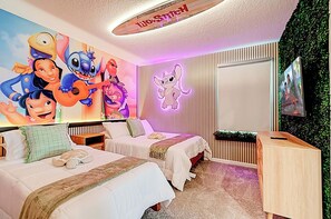 Quarto de hotel com duas camas, um mural animado grande na parede, um letreiro de neon e uma televisão na parede.