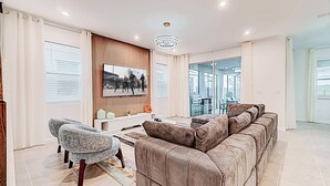 Una sala moderna con un amplio sofá modular, un sillón pequeño, un televisor de pantalla plana montado en la pared y un vidrio que da a un balcón.