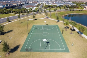 Vue aérienne d’un terrain de basket entouré d’un quartier résidentiel avec des maisons, une route et une étendue d’eau.