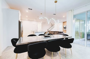 Uma sala de jantar moderna com mesa de vidro, cadeiras pretas e um lustre singular.