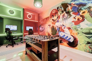 Quarto com mesa de pebolim, dois monitores e um mural temático do Mario.