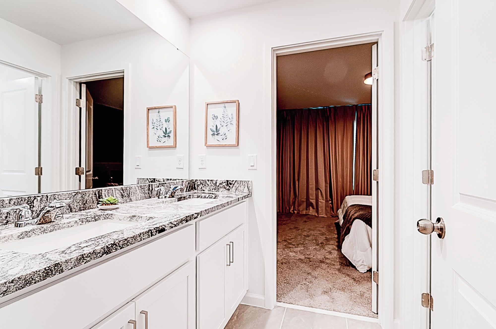 A hotel bathroom with a marble countertop, a large mirror, and framed artwork on the wall.