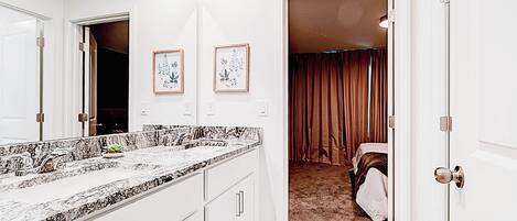 A hotel bathroom with a marble countertop, a large mirror, and framed artwork on the wall.