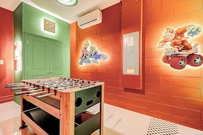 Quarto com mesa de futebol de mesa, paredes verdes e vermelhas e um mural com um personagem de desenho animado.