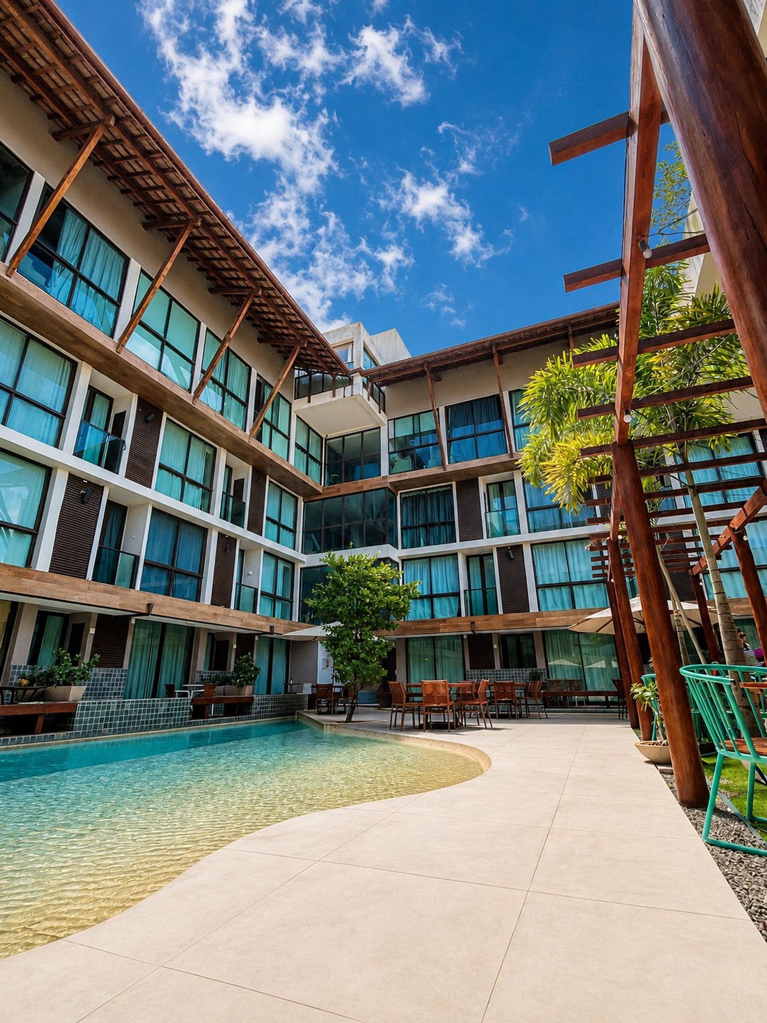 Une cour d’hôtel avec une piscine, des espaces de détente en plein air et un immeuble à plusieurs étages doté de grandes fenêtres.