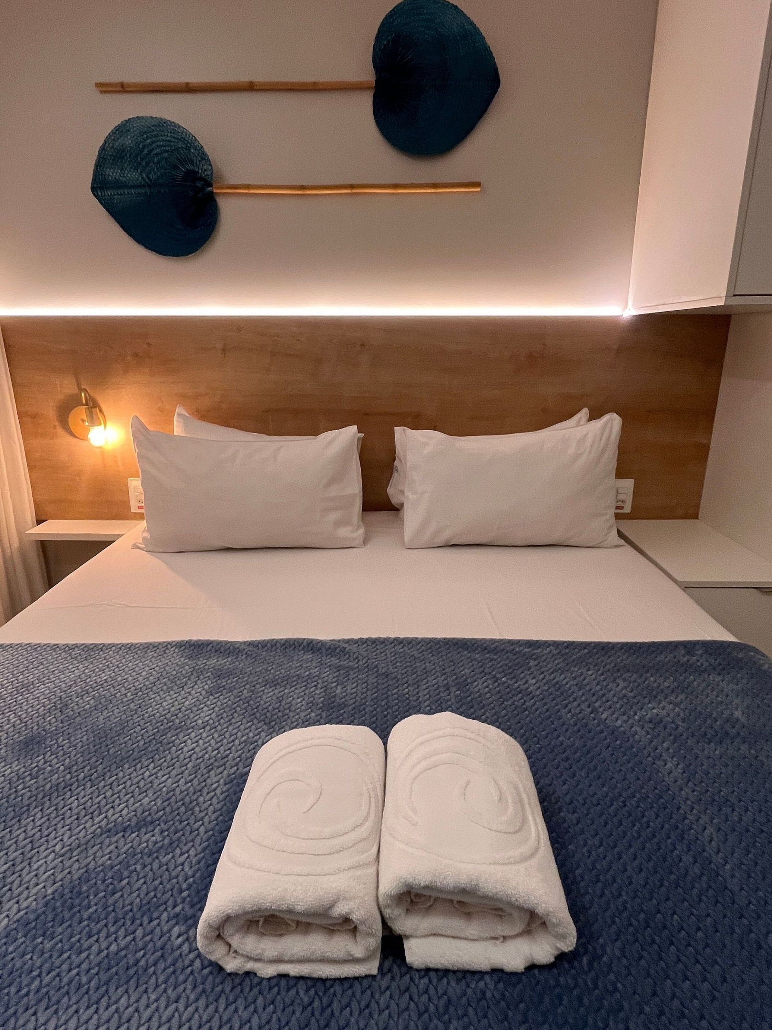A neatly made bed with white linens, two pillows, and a folded towel on a textured blue blanket.