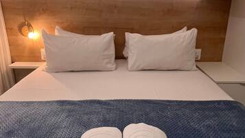 A neatly made bed with white linens, two pillows, and a folded towel on a textured blue blanket.