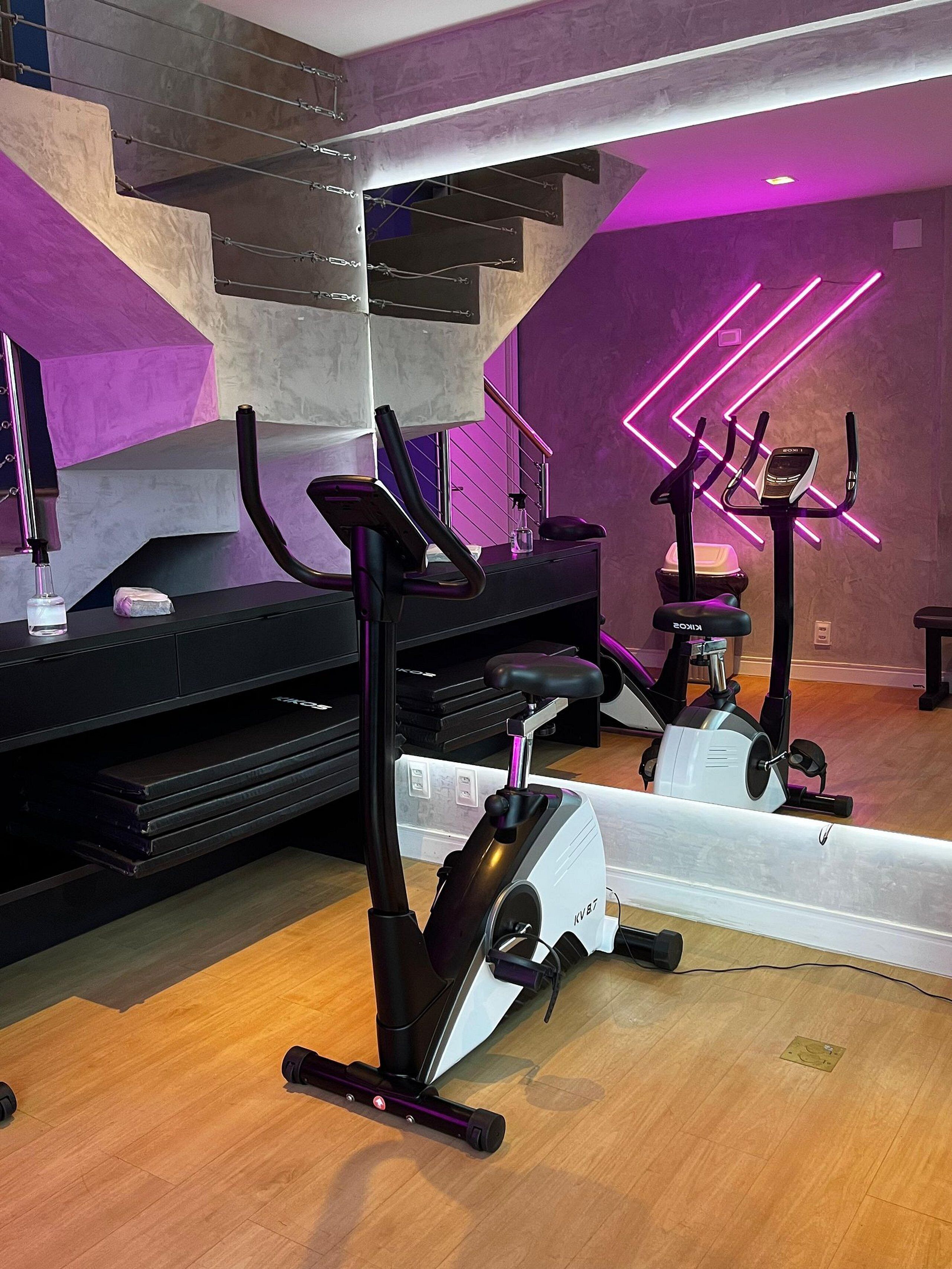Een sportschool thuis met trainingsapparatuur, een trap en een paars verlichte muur.