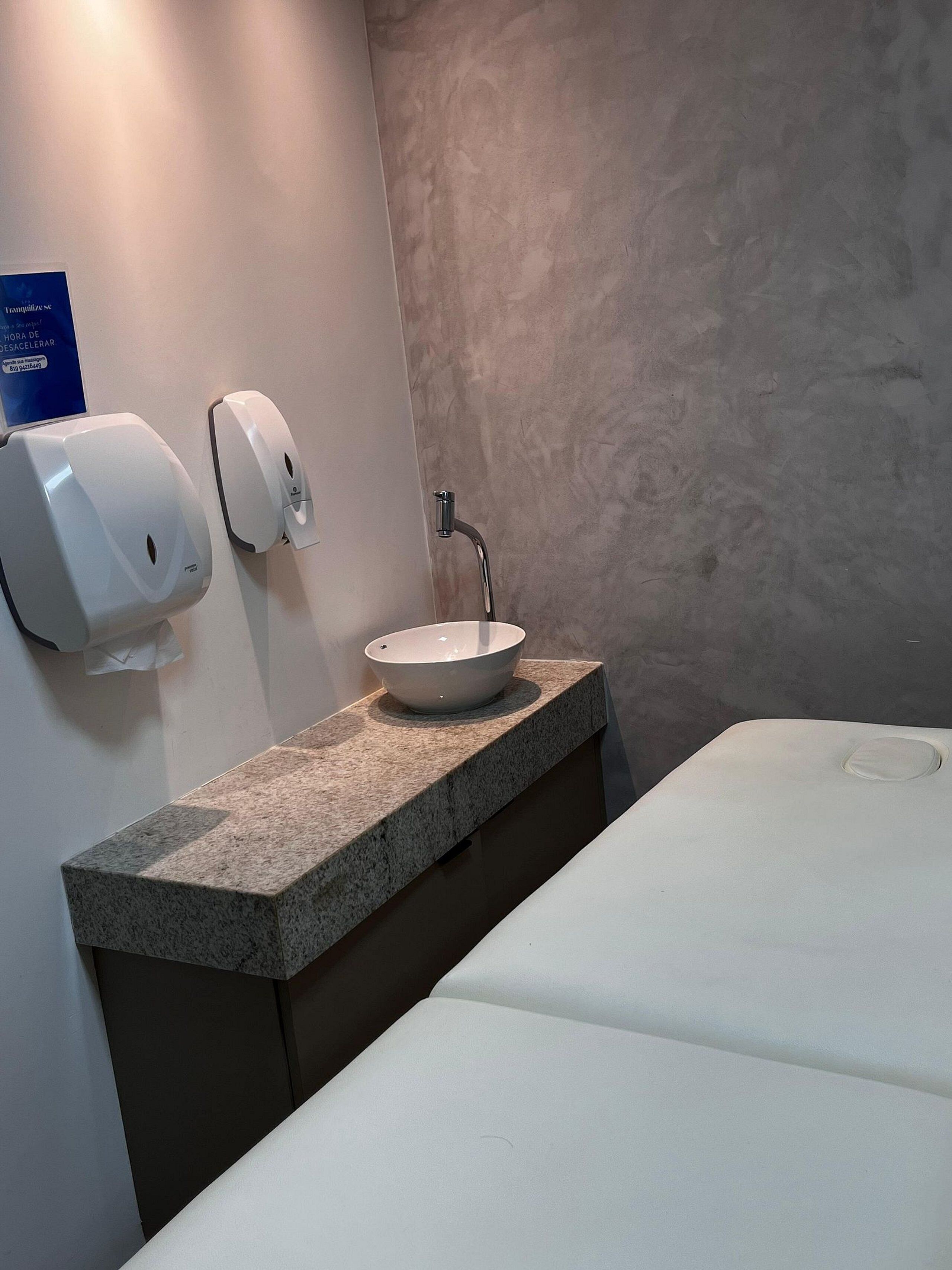 Casa de banho moderna com bancada de granito, lavatório branco e dispensador de papel.