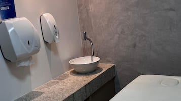 Casa de banho moderna com bancada de granito, lavatório branco e dispensador de papel.