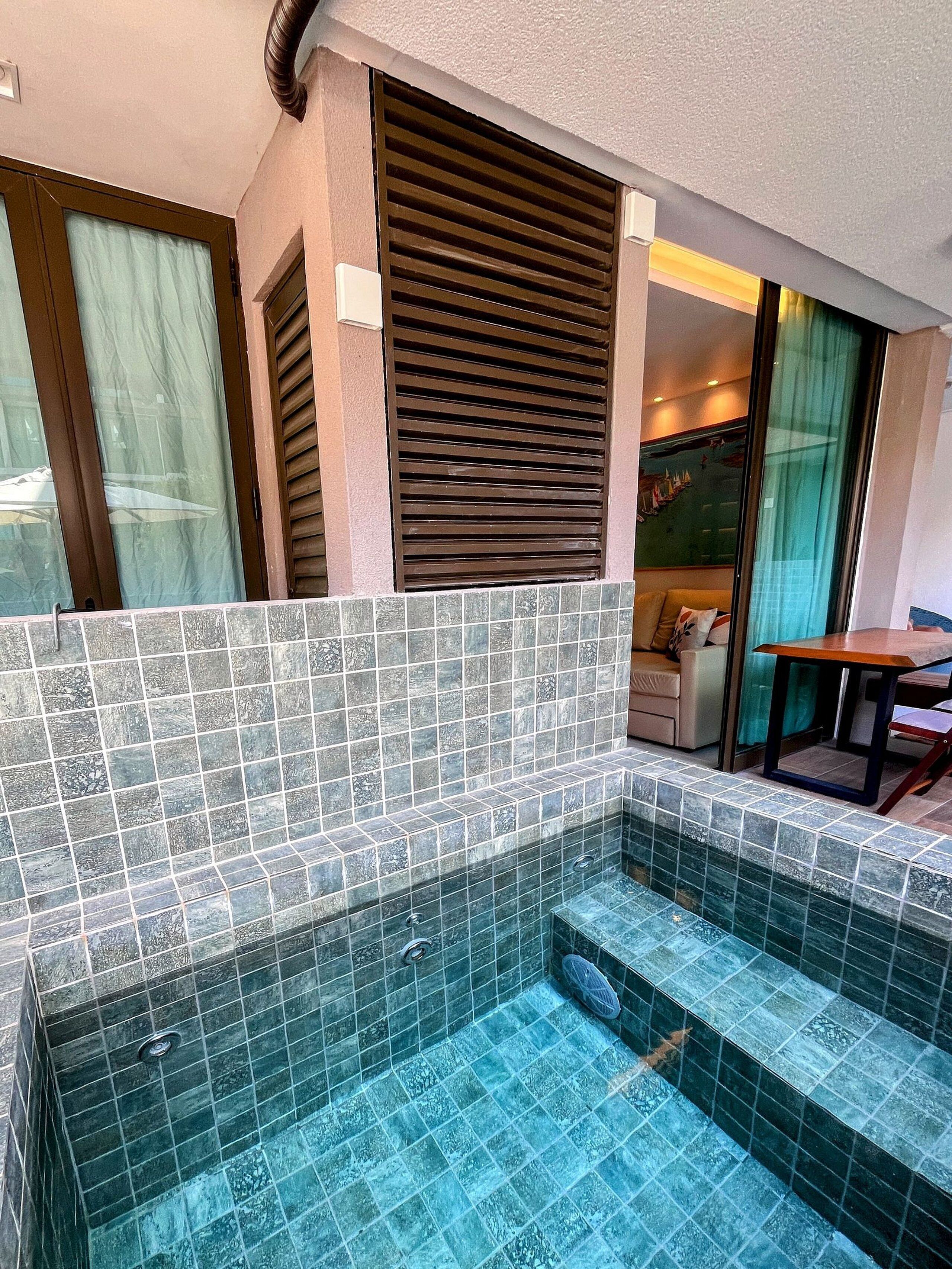 A small indoor pool with tiled walls and steps leading into it, a sofa, and a table in the background.