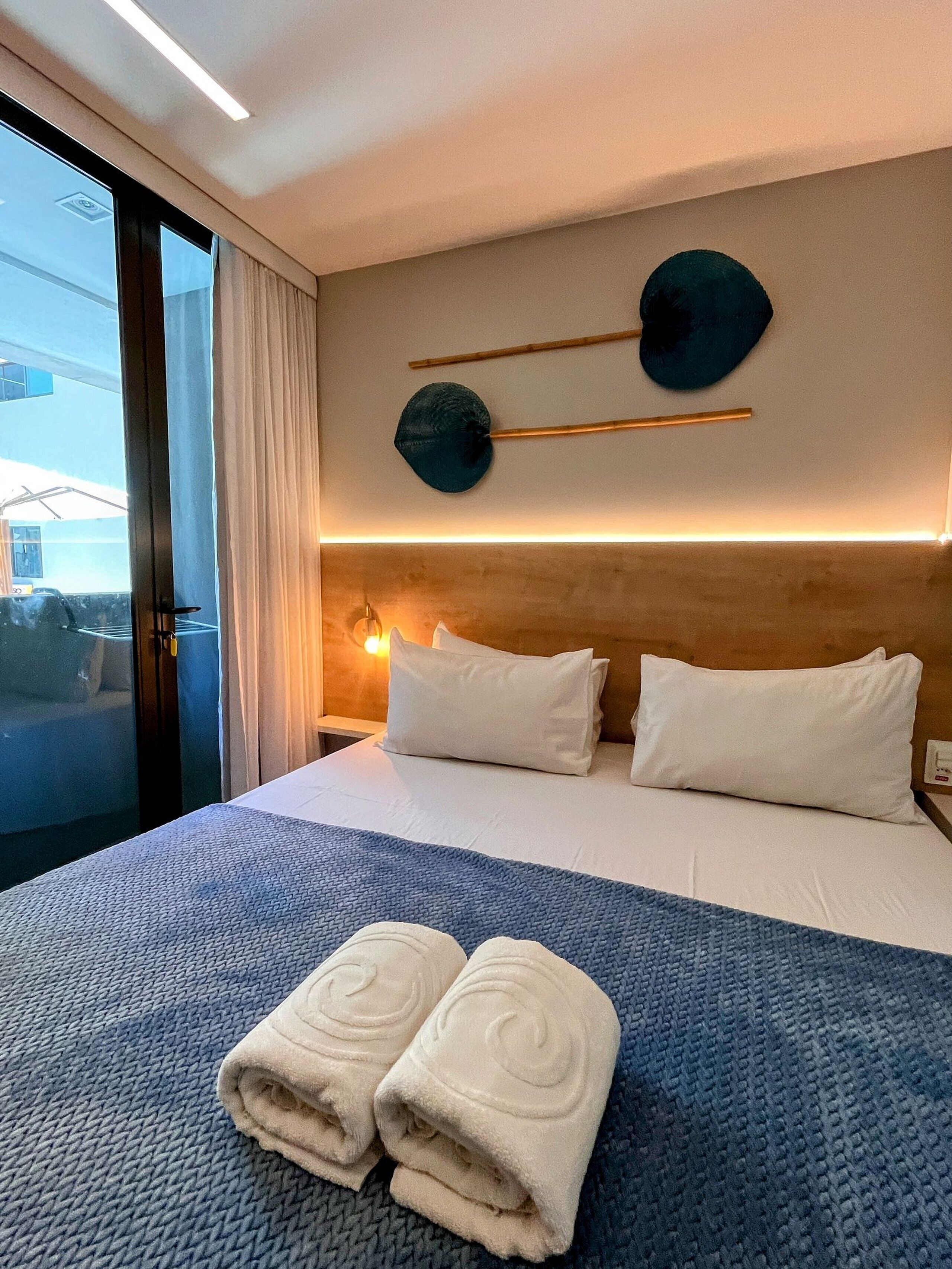 Quarto de hotel com uma cama, almofadas, um cobertor azul texturizado e um par de toalhas.