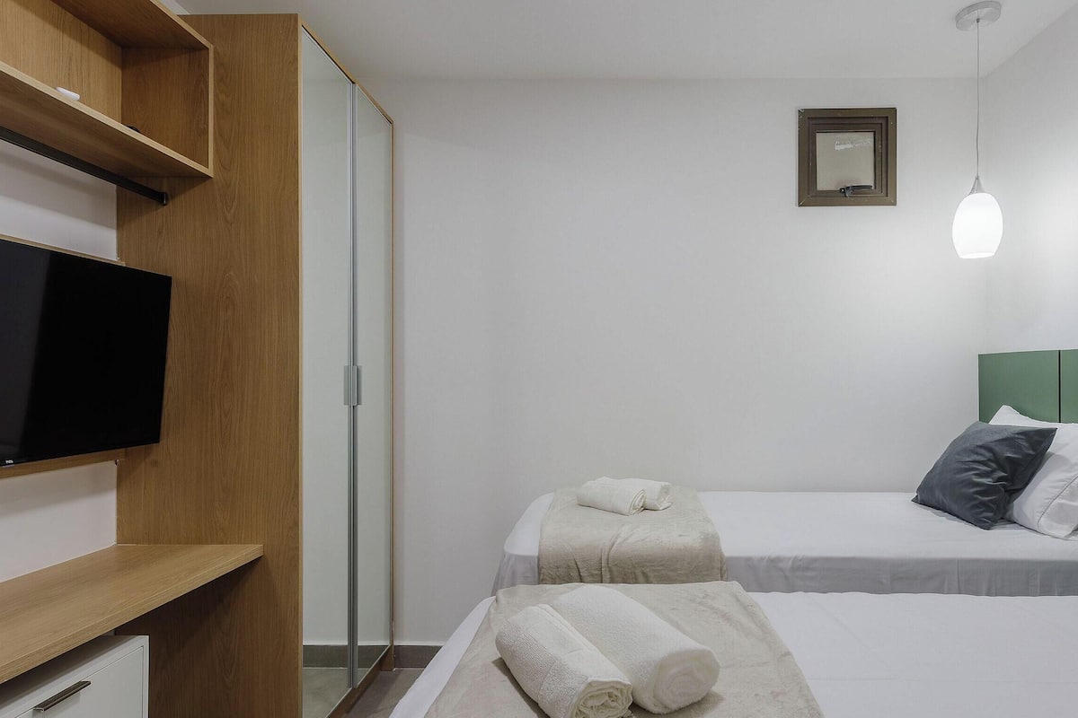 A hotel room with a TV, two beds, a green headboard, and a shower.