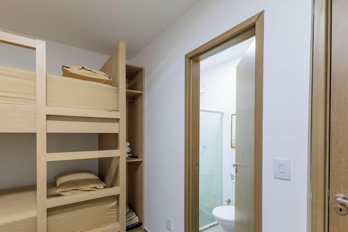 A room with a bunk bed, a bathroom with a toilet and shower, and a door leading to another room.