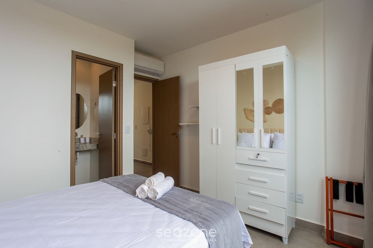 A bedroom with a bed, a wardrobe, a mirror, and a towel rack.