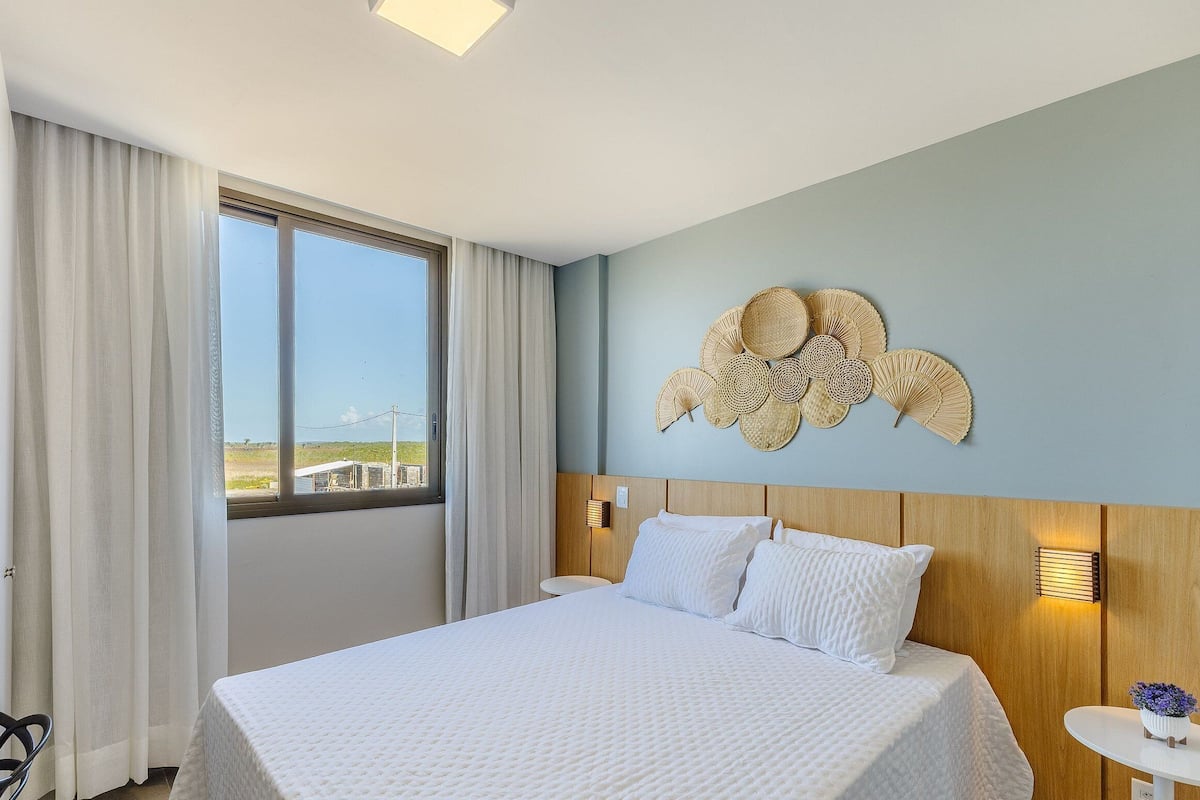 A hotel room with a large bed, a view through the window, and a decorative wall piece.