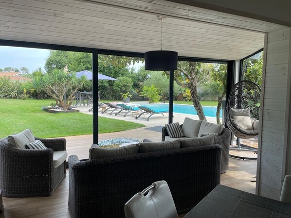 Uma área externa moderna com móveis de vime, uma cadeira suspensa e vista para uma piscina.
