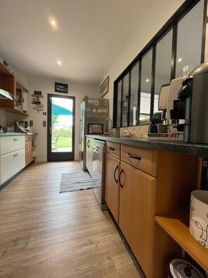 Cozinha moderna com armários de madeira, forno embutido, máquina de café e vista para o exterior através de uma porta de vidro.