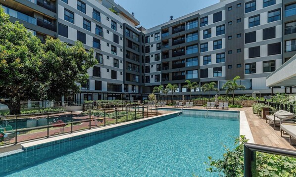 Un bâtiment moderne doté d’une piscine, entouré de verdure et offrant des espaces de détente en plein air.