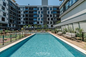 A swimming pool with lounge chairs and a view of a modern apartment building.