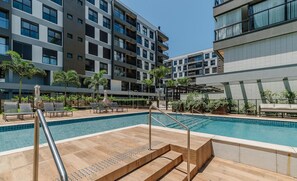 A modern pool area with a clear blue pool, sun loungers, and a staircase leading to the pool.