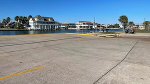 A waterfront property with a large open parking area, a building with multiple balconies, and a small boat docked nearby.