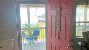 A room with a red door, a white cabinet, a glass door leading to an outdoor patio with a blue chair, and a small table with a bag on it.