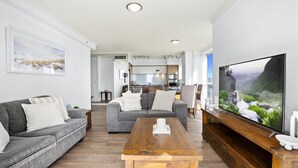 Een moderne woonkamer met een grijze bank, een houten salontafel en een grote flatscreen-televisie.