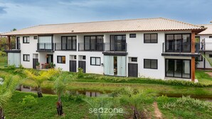 A modern two-story house with a tiled roof, large windows, and a balcony. - VLP - Apartments Close to Praia do Forte/ba (Mata de São João)