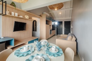 A modern living room with a TV, sofa, dining table set, and kitchen area. - VLP - Apartments Close to Praia do Forte/ba (Mata de São João)